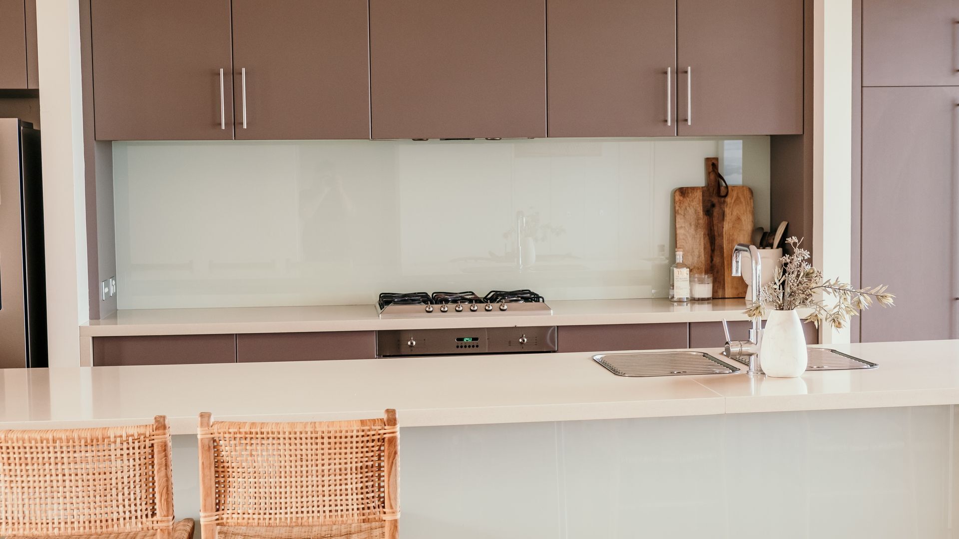 A modern kitchen with a central island, stainless steel appliances, and wicker chairs.