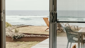 A view from a room with a sliding glass door overlooking a beach with chairs and a table. - Hearns Beachside Villa 9 (Port Fairy)