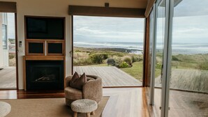 A modern living room with a fireplace, a comfortable seating area, and a large glass door leading to a deck with a view of the ocean. - Hearns Beachside Villa 9 (Port Fairy)