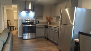 A modern kitchen with stainless steel appliances, grey cabinetry, and a wooden floor.