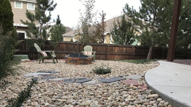 A backyard with a stone fire pit, a wooden fence, and a paved area with chairs.