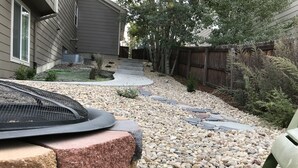 A garden pathway with stepping stones, a small fire feature, and a wooden fence.