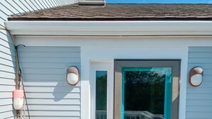 A white building with a teal door and a small window. There are colorful buoys hanging on the side. - NEWLY RENOVATED, LARGE, SERENE, SUNNY  HOME ON PRIVATE ROAD (North Truro)