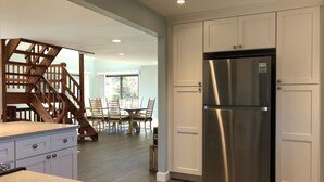 A modern kitchen with a stainless steel refrigerator, wooden staircase, and a dining area with chairs. - NEWLY RENOVATED, LARGE, SERENE, SUNNY  HOME ON PRIVATE ROAD (North Truro)