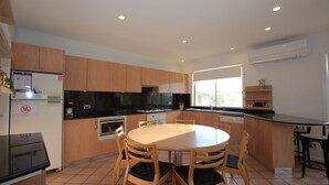 A modern kitchen with wooden cabinets, a black countertop, a built-in oven, and a dining area with a round table and chairs.
