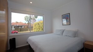 A bedroom with a large window, a bed with white bedding, a small bedside table, and a radiator.