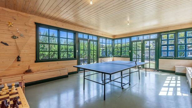 Une pièce spacieuse avec une table de ping-pong, de grandes fenêtres et un jeu d’échecs posé sur le sol.