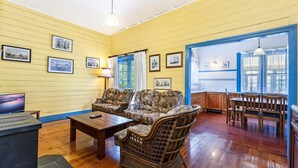 Une pièce aux murs recouverts de bois, avec un canapé, une table à manger et des chaises. Des tableaux encadrés ornent les murs et une lampe se trouve sur la table.