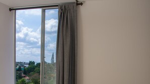 Une chambre avec une grande fenêtre, un lit avec une literie grise et une vue sur la verdure.