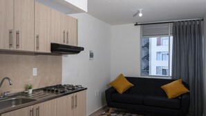 Une cuisine moderne avec des meubles en bois, une cuisinière à gaz et un canapé noir agrémenté de coussins couleur moutarde.