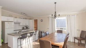 Een moderne keuken met witte kastjes, een houten eettafel en een kroonluchter.