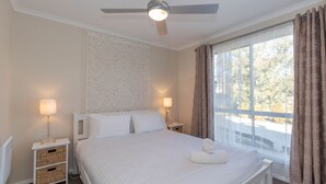 Een slaapkamer met een bed, twee bedlampen, een plafondventilator en een raam met gordijnen.
