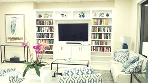 A living room with a flat-screen TV, bookshelves, patterned furniture, and decorative items.