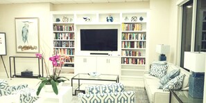 Uma sala de estar com televisão de tela plana, estantes de livros, móveis estampados e objetos decorativos.
