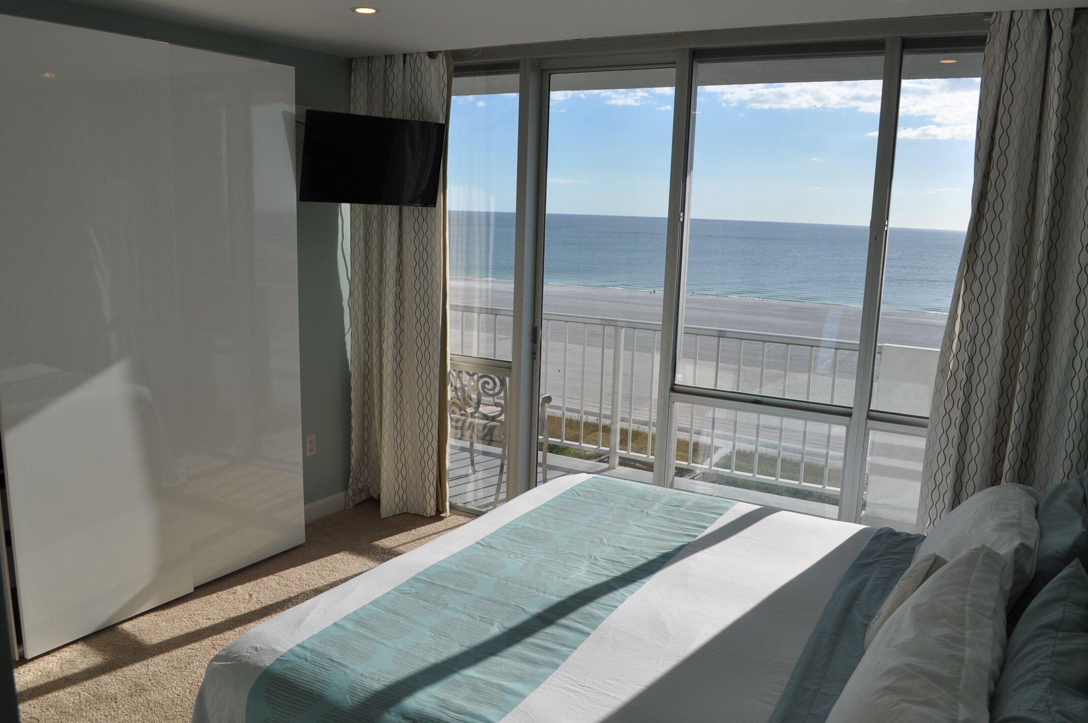 Ein Schlafzimmer mit einem großen Bett, einem an der Wand montierten Fernseher und einem Balkon mit Blick auf den Strand.