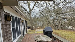 A wooden deck with a table and chairs, a barbecue grill, and a covered bench area. - Menemsha Home Fully Renovated w/ Amazing Waterview's of Vineyard Sound (Menemsha)