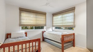 Ein Zimmer mit zwei Betten, einem Deckenventilator und großen Fenstern mit Jalousien.