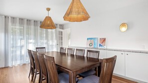 A dining area with a wooden table and chairs, two wicker pendant lights, a white cabinet, and a framed artwork on the wall.