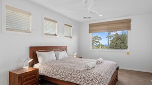 Un dormitorio con cama, mesita de noche, lámpara, ventilador de techo y ventana con vistas.