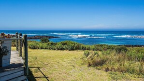 A coastal view with a wooden deck, grassy area, and ocean waves. - Wytonia 2 - Ocean Views From Your Bed (Port Fairy)