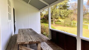 Taula i banc de fusta en un porxo amb vista a una zona verda i arbres.