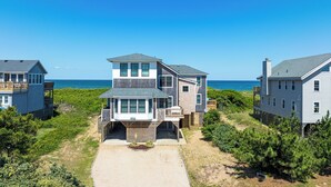 Ein zweistöckiges Strandhaus mit Balkon, überdachter Veranda und Blick aufs Meer.