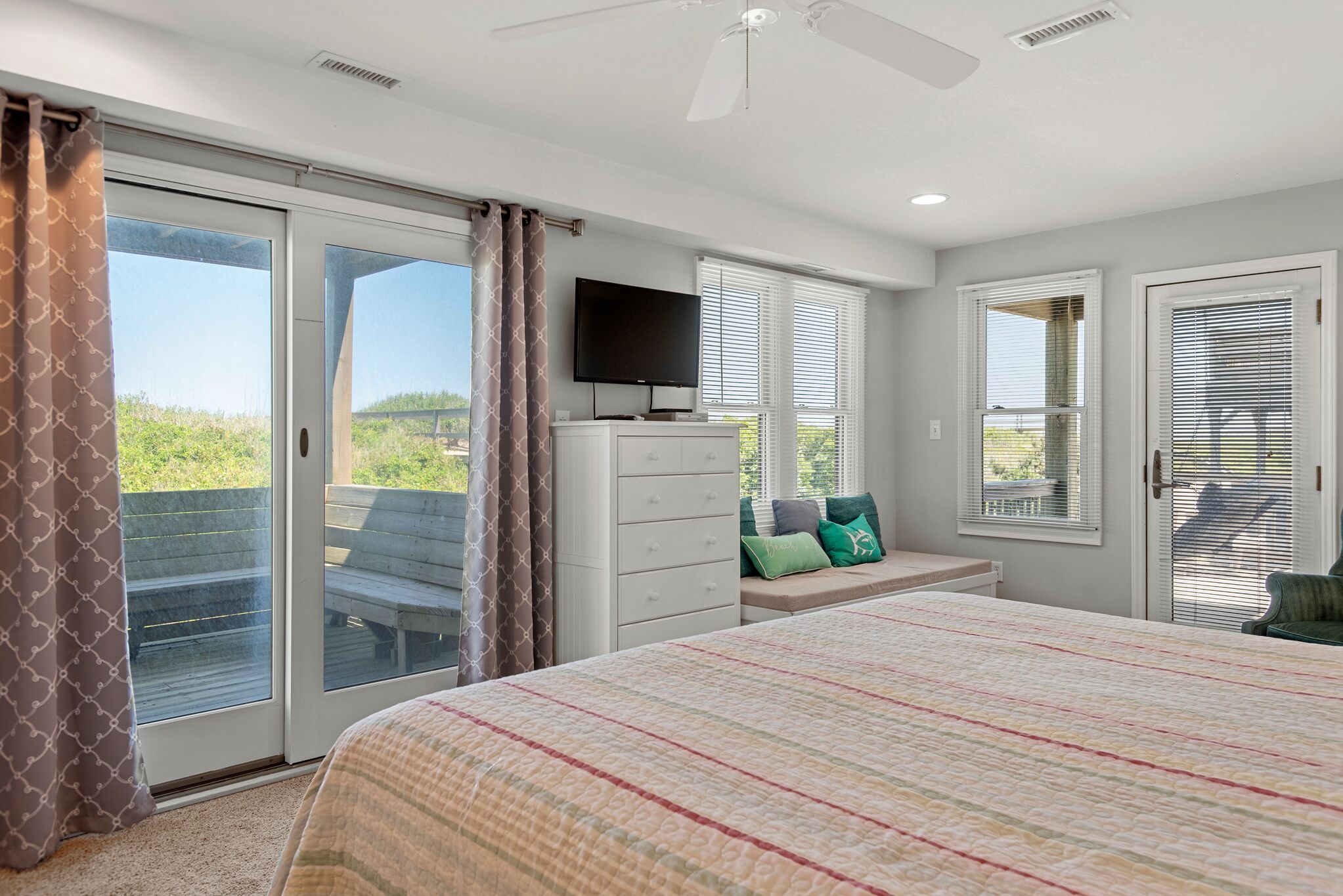 A bedroom with a large bed, a TV, a dresser, and a bench with pillows.