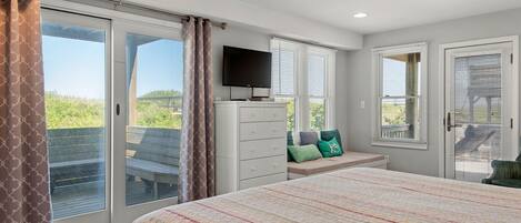 A bedroom with a large bed, a TV, a dresser, and a bench with pillows.