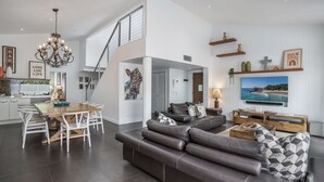 A spacious living area with a dining table, a leather sofa, a TV, and a staircase.