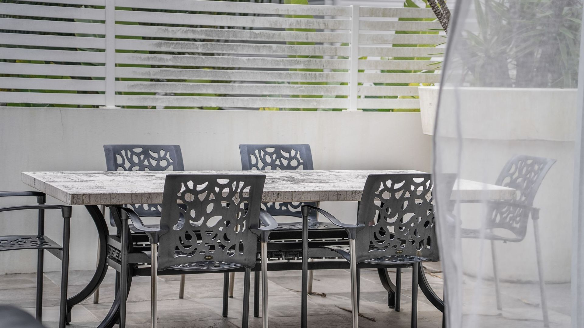 An outdoor patio with a wooden table and chairs, a white fence, and a clear view of the sky.