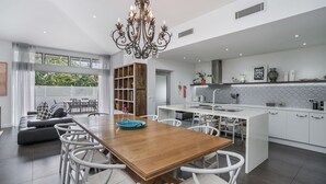 A modern kitchen with white cabinetry, a central island, and a dining area with a wooden table and white chairs.