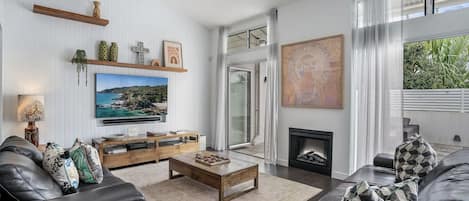 A modern living room with a flat-screen TV, a fireplace, and a large window offering a view of greenery.