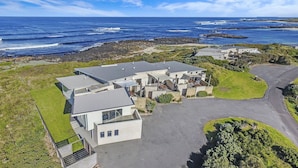 A coastal residential area with modern houses, a paved driveway, and a rocky shoreline. - Hearns Beachside Villa  7 (Port Fairy)