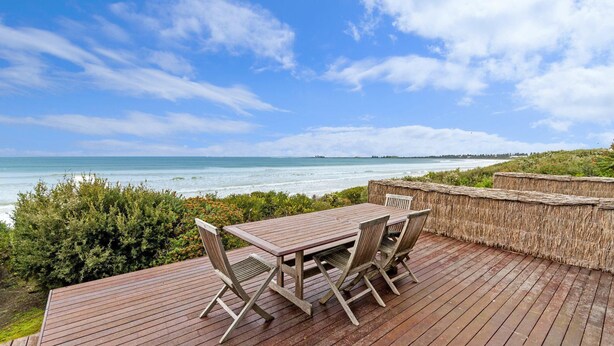 Une terrasse en bois avec une table et des chaises donnant sur une plage.