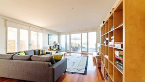 Un salon spacieux avec un canapé gris, une bibliothèque en bois et une grande fenêtre donnant sur l’extérieur.
