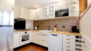 A modern kitchen with white cabinets, a brick backsplash, and stainless steel appliances including a refrigerator, stove, and dishwasher. - Heidelburg - 3/6 Banjo Patterson Crescent (Jindabyne)