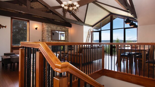 A spacious interior with a wooden staircase, stone walls, and large windows offering a view of the outdoors. - Heidelburg - 3/6 Banjo Patterson Crescent (Jindabyne)