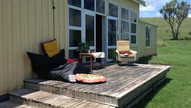 A wooden deck with a sofa and cushions, a chair, and a table with a plant.