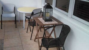 Un pequeño patio con una mesa redonda y cuatro sillas, un farol y un ventanal grande.