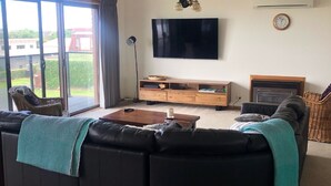 Ein Wohnzimmer mit einem großen schwarzen Sofa, einem Holztisch, einem an der Wand befestigten Fernseher und einem Kamin.