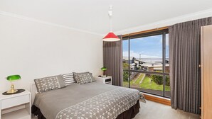 Ein Schlafzimmer mit einem großen Bett, einem Nachttisch, einer Lampe und Blick ins Freie.