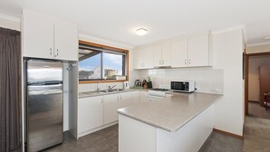 Eine moderne Küche mit weißen Schränken, Edelstahlgeräten, einem großen Fenster und Blick ins Freie.