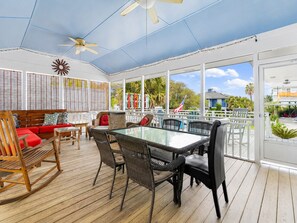 Un espace extérieur abrité, doté d’une table et de chaises en verre, d’un banc en bois et d’un ventilateur de plafond.