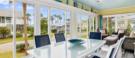 A sunlit room with a glass table, white chairs, and a view of the neighborhood.