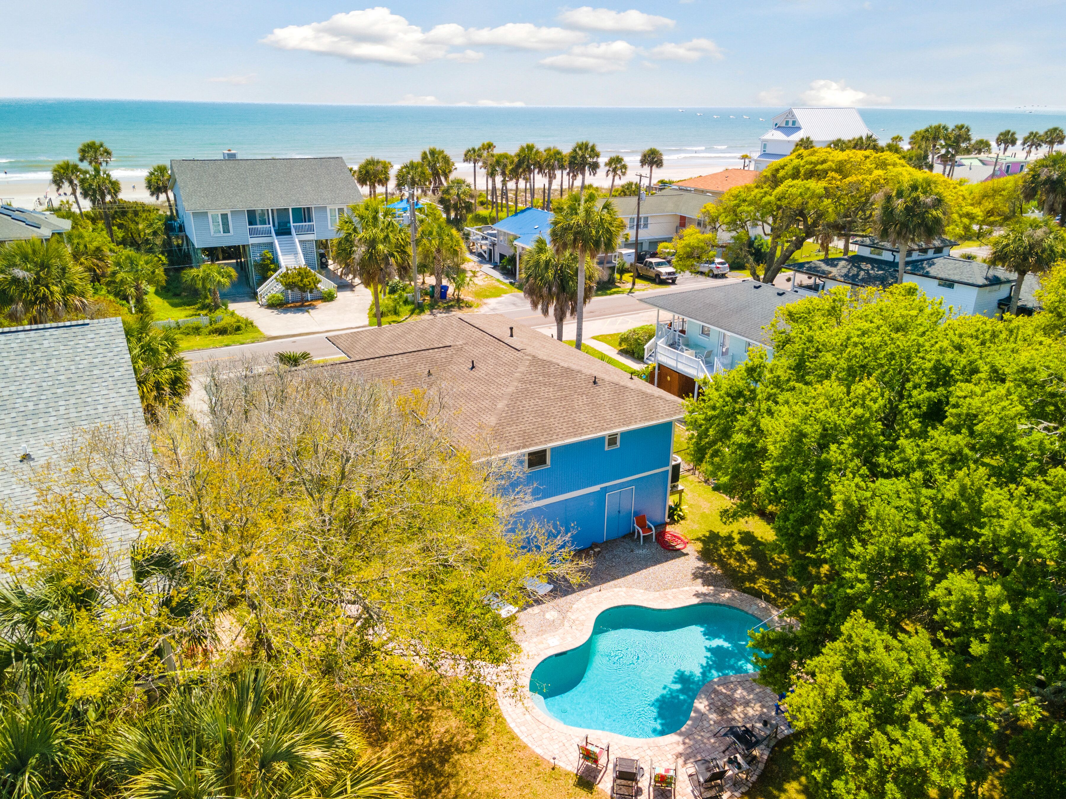 A residential area with a swimming pool surrounded by lush greenery and a view of the ocean.