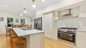 A modern kitchen with a central island, stainless steel appliances, and wooden chairs. - 15 Esprit Drive - Rainbow Shores. Wifi. Close to beach (Rainbow Beach)