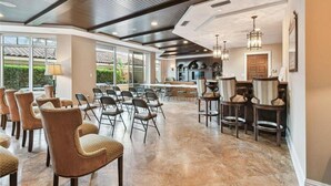A spacious room with a high ceiling, large windows, and a mix of seating arrangements including chairs and bar stools.