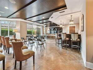 A spacious room with a high ceiling, large windows, and a mix of seating arrangements including chairs and bar stools. - Belle Harbor 401W Belle Harbor Jewel (CLearwater Beach)
