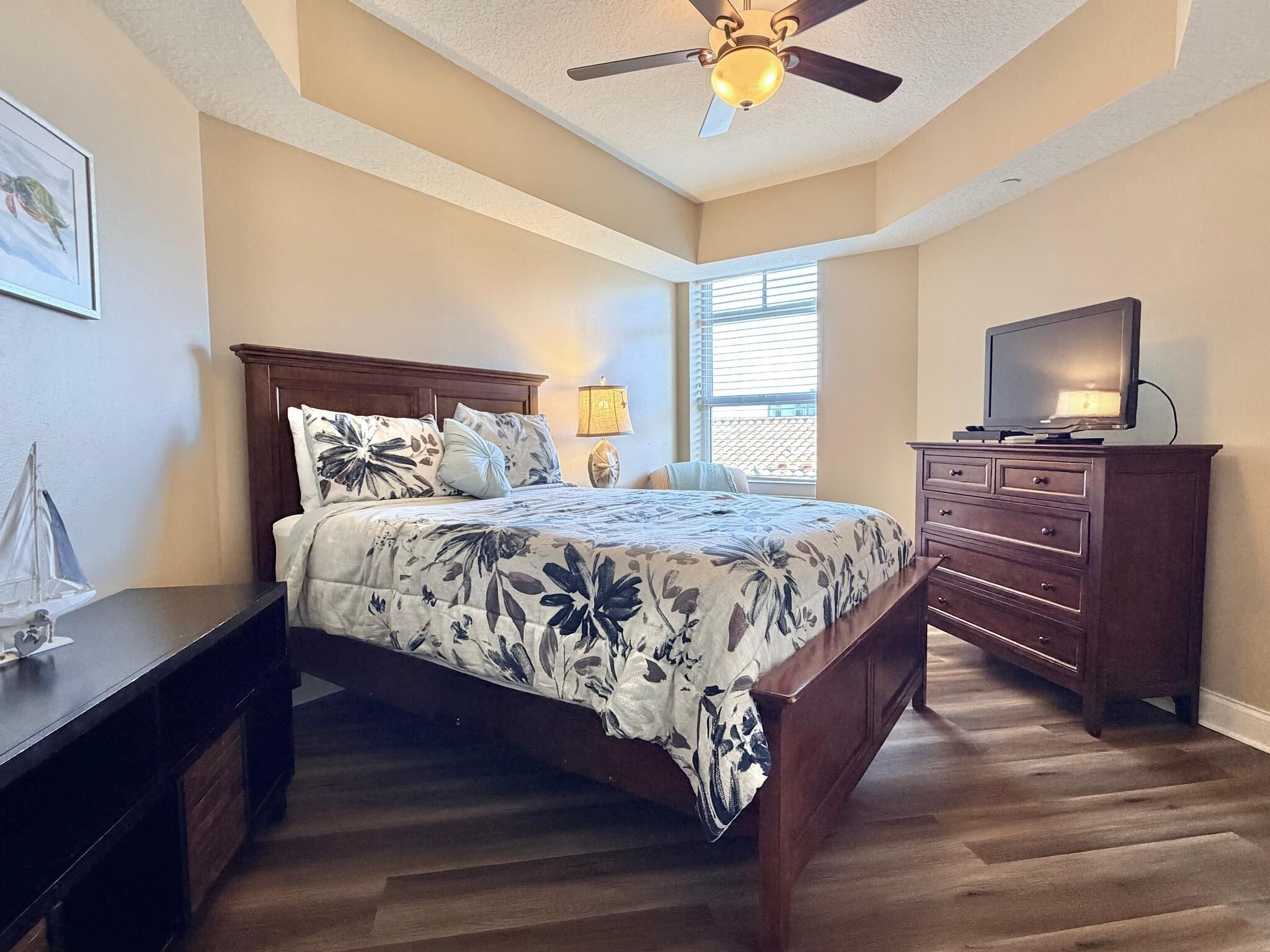 A bedroom with a bed, dresser, TV, and a ceiling fan.