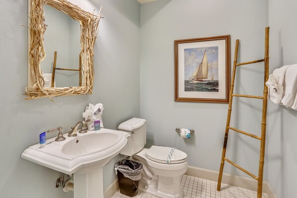 Une salle de bain avec un lavabo, des toilettes et un tableau encadré représentant un voilier accroché au mur.